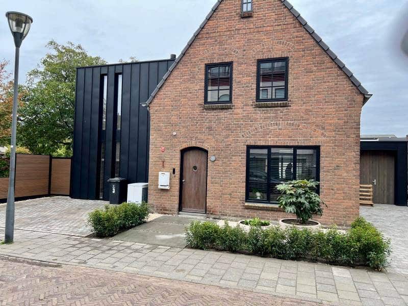 Voorgevel verbouwde woning in Waalwijk met kasseien oprit en strakke aanbouw in zwart zink