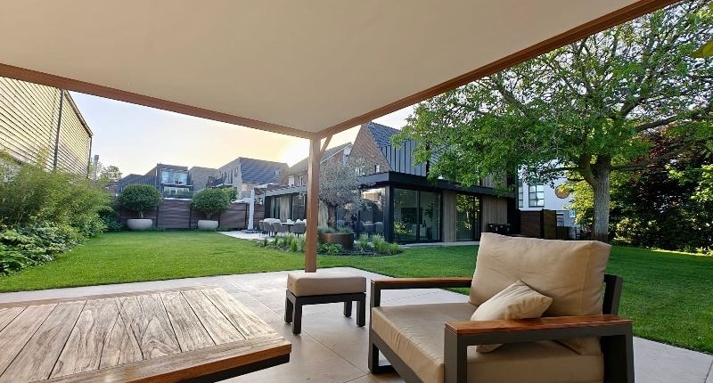 loungedeelte-tuin-overkapping-waalwijk Loungedeelte onder overkapping met zicht op de achtertuin in Waalwijk