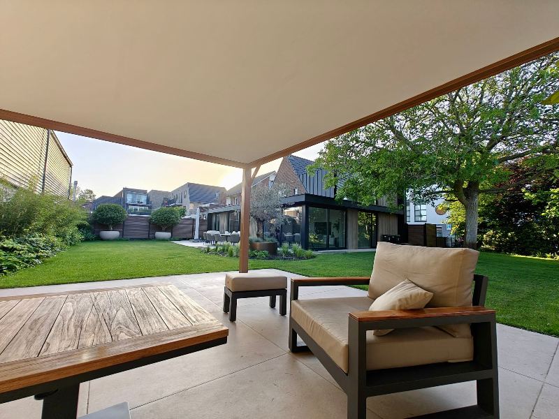 loungedeelte-tuin-overkapping-waalwijk Loungedeelte onder overkapping met zicht op de achtertuin in Waalwijk