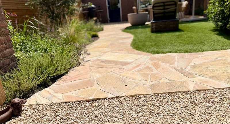 slingerend-tuinpad-flagstones-border-kunstgras-terras Slingerend tuinpad van flagstones tussen border en kunstgras naar terras